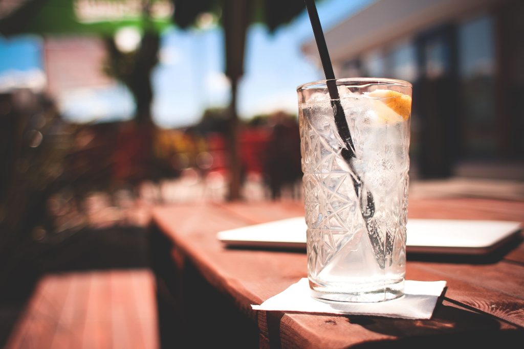 A refreshing tropical cocktail with ice cubes on a wooden table at a Cancun resort with a blurry swimming pool background