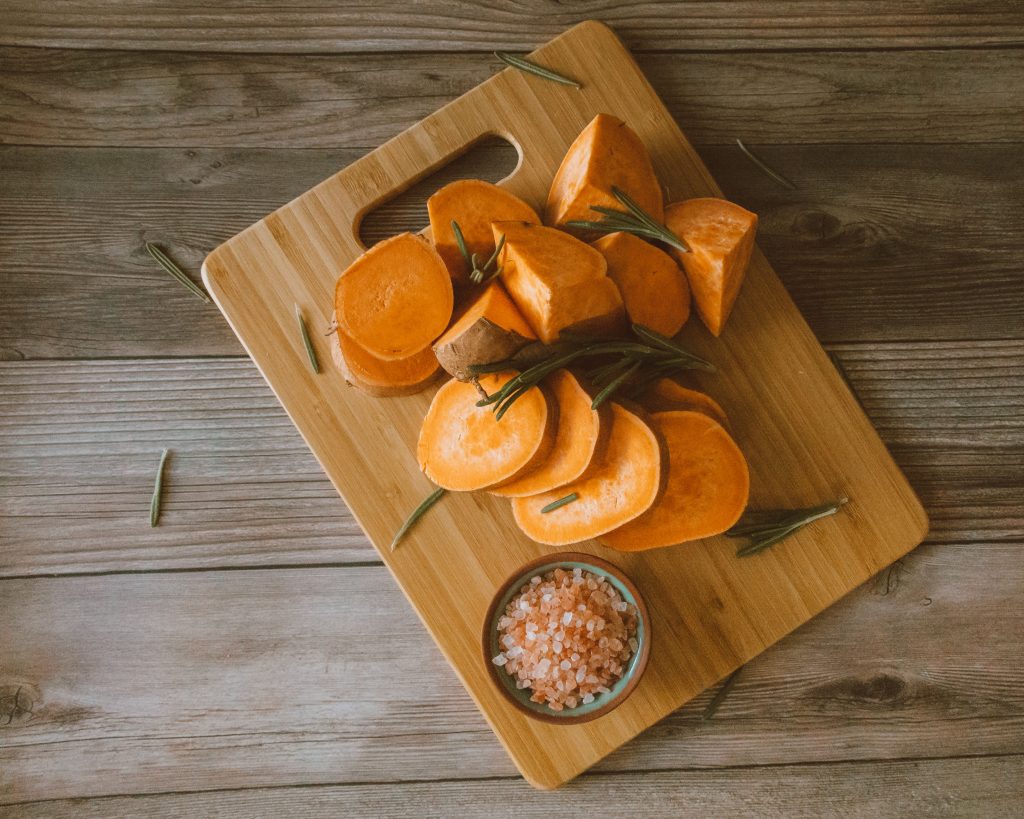 A halved fresh lemon and coarse sea salt being used to clean and sanitize a bamboo cutting board.