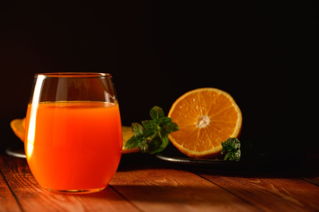 glass of fresh orange juice next to a halved orange and mint leaves on a wooden table