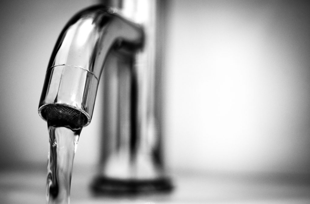 Close-up of fresh running tap water pouring directly from a metal kitchen faucet into a clear glass.