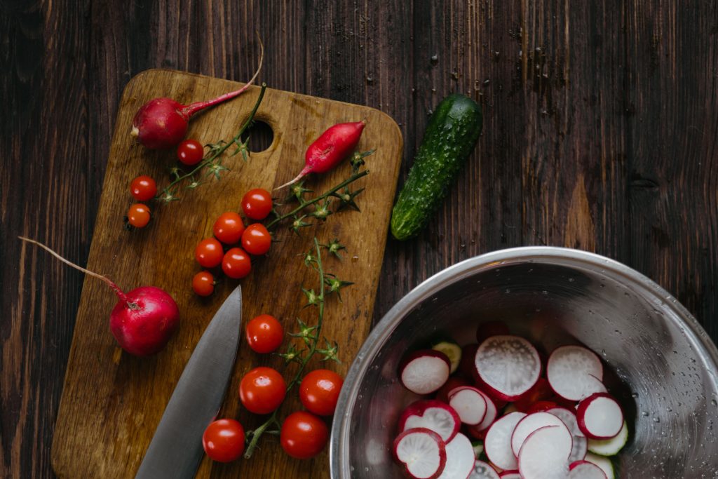 Fresh organic vegetables being chopped on a premium wooden end-grain cutting block in a bright kitchen.